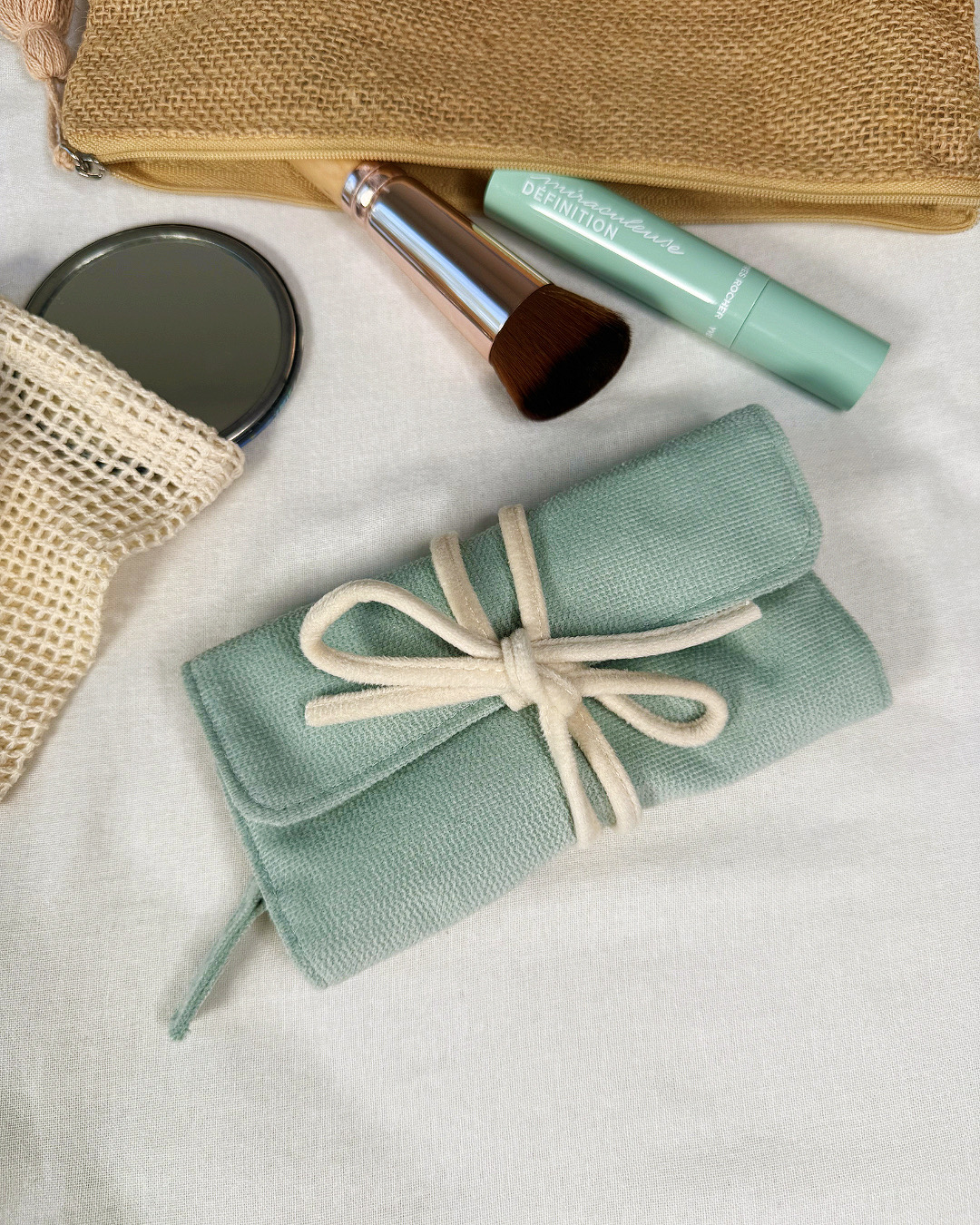 Trousse bijoux roulée verte fermée, présentée avec accessoires beauté